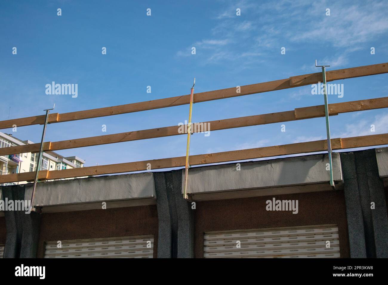 Fallschutzgerüst auf einer Baustelle. Dach mit Holzgeländern an der Dachkante, die an den Dachtrassen des Gebäudes eingehakt sind. Stockfoto