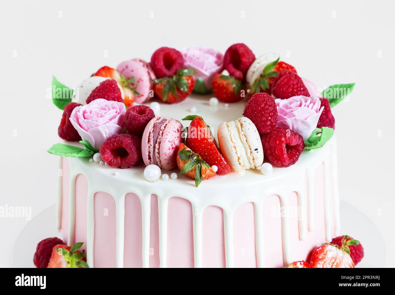 Süßer Geburtstagskuchen mit Beeren, Makronen und Blumendekor auf dem Tisch. Wunderschöner rosa Kuchen dekoriert mit Makronen, Himbeeren, Erdbeeren und Zucker Stockfoto