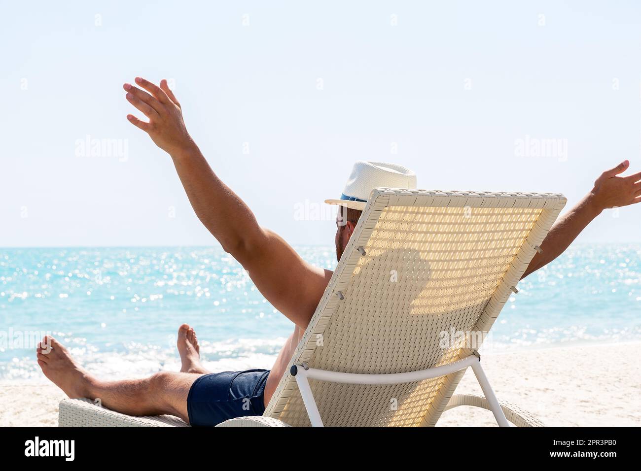 Junger Mann mit weißem Hut, der sich auf einem Liegestuhl am wunderschönen Sandstrand entspannen kann. Sommerferienkonzept. Mann entspannt am Strand, Meerblick, Dominikanische Republik Stockfoto