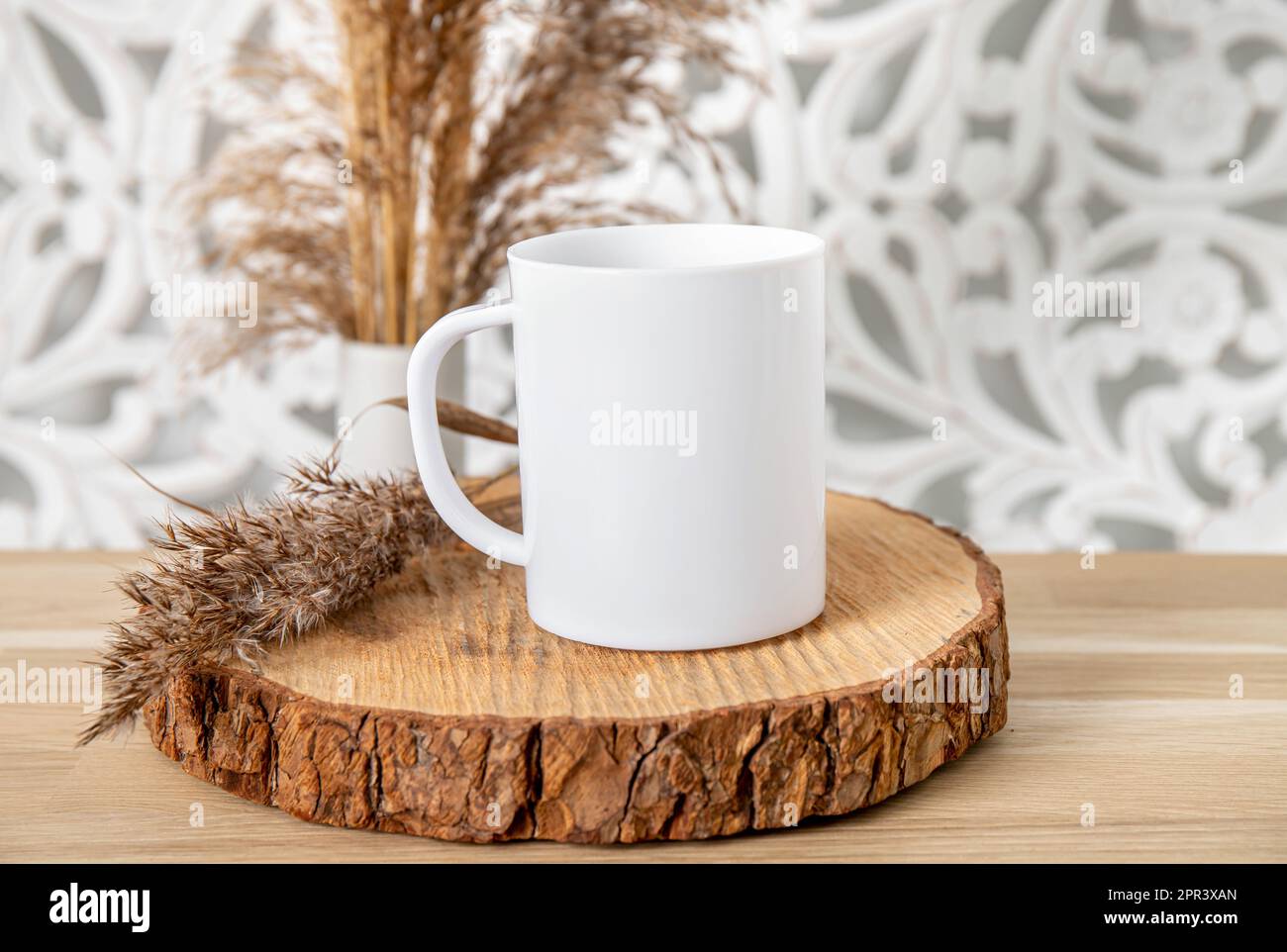 Ein weißes, leeres Tassenmodell im Wohnzimmer. Eine Tasse auf einem Holztisch mit trockener Schilfpflanzendekoration. Viel leerer Kopierspeicher. Stockfoto