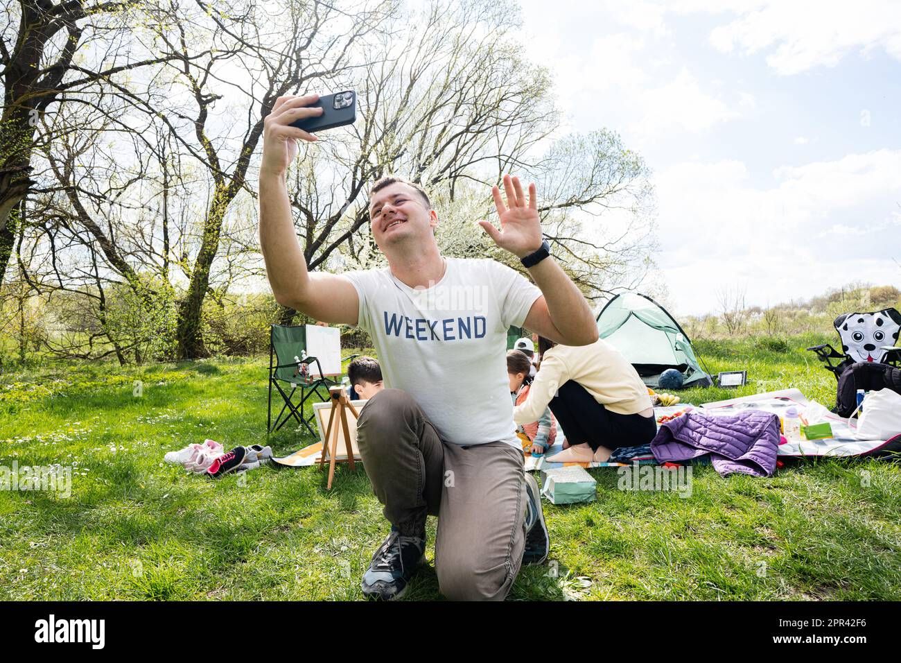 Dad leitet einen Vlog. Glückliche junge Familie, die Spaß hat und draußen auf einer Picknickdecke im Garten Spring Park, Entspannung. Stockfoto