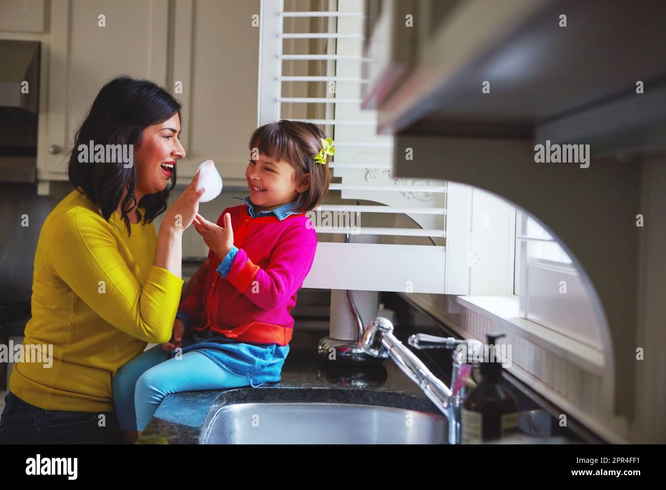 Blitzsauber, spitz und glitzernd. Eine junge Mutter und ihre Tochter, die am Waschbecken spielen. Stockfoto