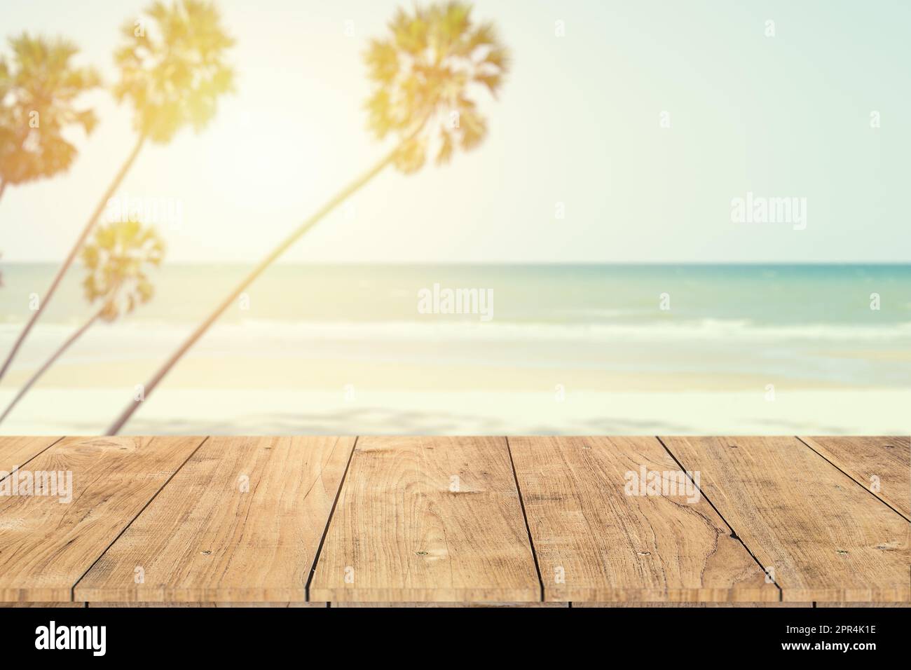Sommerpalme am Strand mit Holztisch im Vordergrund zur Werbung für Produkte Montage Hintergrund Vintage Farbton Stockfoto