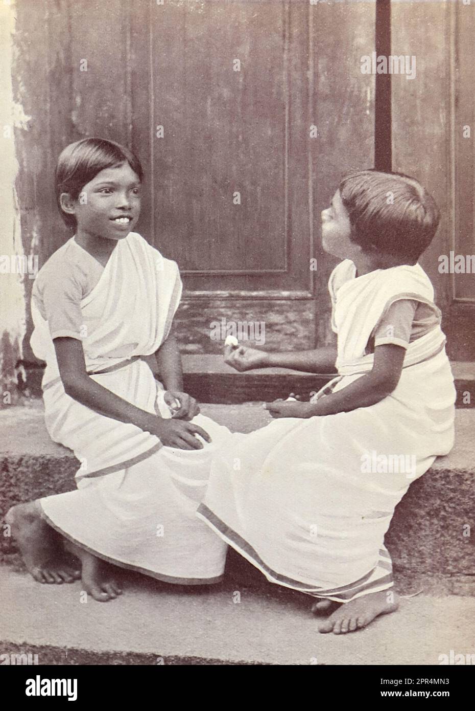 Zwei Indianermädchen, die mit Kieseln spielen. In der Dohnavur-Anlage. Halbtongravierung auf einem Foto von Mr. Penn aus Ootacamund (jetzt bekannt als OOTO), in der Region Tamil Nadu in Südindien, c1912. Das Bild bezieht sich auf das Kinderzimmer und das Gelände der Church of England Zenana Mission in Dohnavur, ebenfalls in Tamil Nadu und etwa 30 Meilen von der Südspitze Indiens entfernt. Das Gelände wurde von Amy Wilson-Carmichael betrieben und versuchte, das Christentum bei Babys und Kindern zu fördern (damals nur Mädchen, von denen viele Opfer der Tempelprostitution waren). Stockfoto