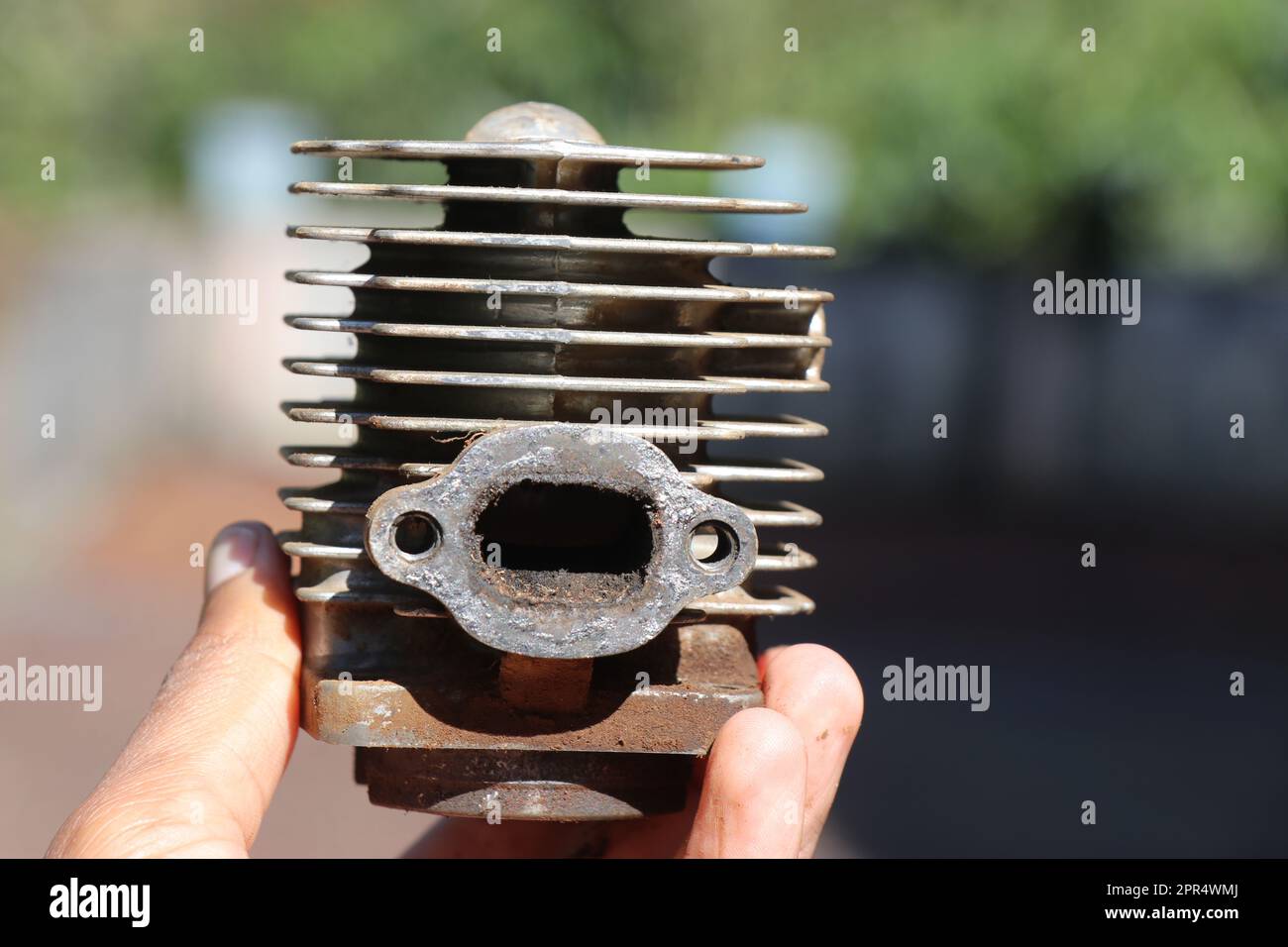 Zylinderkopf des Benzinmotors mit Einlässen und Kühlrippen zerlegt. Kleiner Motorzylinderkopf aus Aluminium mit Benzinmotor, der in der Hand gehalten wird Stockfoto