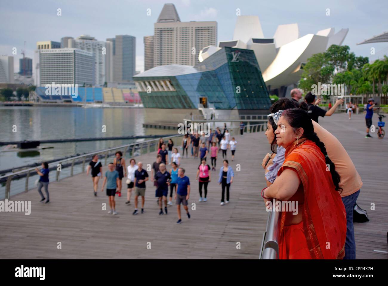 Eine weibliche indische Touristin mittleren Alters und ihre Familie genießen den Blick über Marina Bay, Singapur und das angrenzende Stadtbild Stockfoto