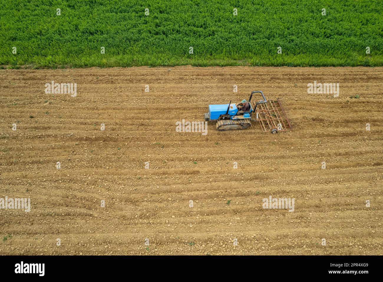 Castell'Arquato, Italien - April 2023 Landwirt, der auf gepflügtem, trockenem Feld einen Raupentraktor fährt, bevor er aus der Vogelperspektive sät Stockfoto