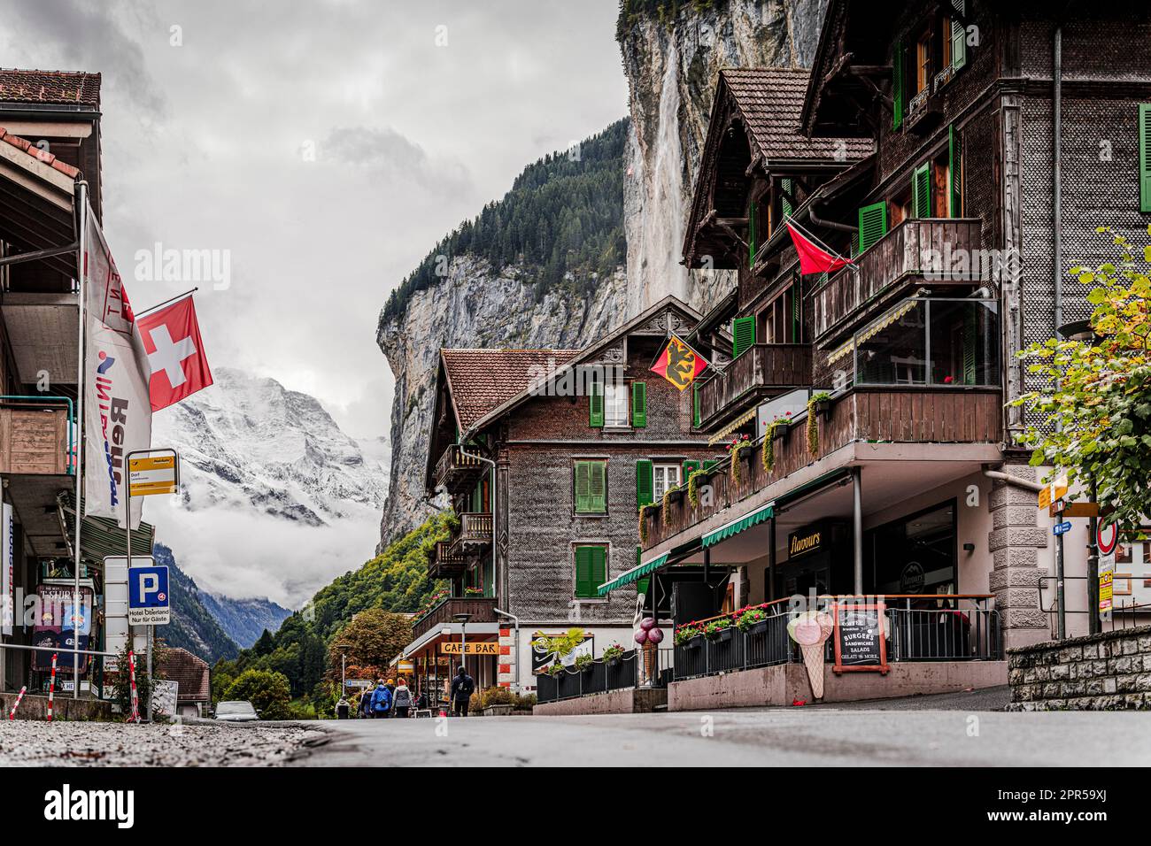 Traditionelle Holzhäuser im Bergdorf Lauterbrunnen mit Trummelbachfällen im Hintergrund, Kanton Bern, Schweiz Stockfoto
