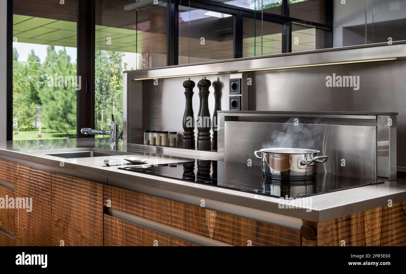 Stahltopf mit kochenden und dampfenden Speisen in moderner Küche aus Holz und Edelstahl. Kochen. Stockfoto