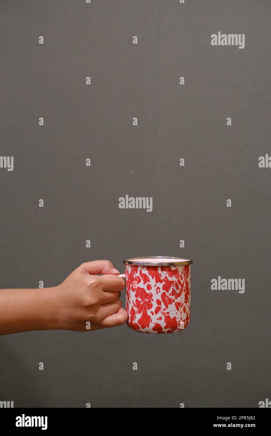 Porträt- oder vertikale Aufnahme einer handgeführten Emaille-Tasse auf dunkelgrauem Hintergrund Stockfoto
