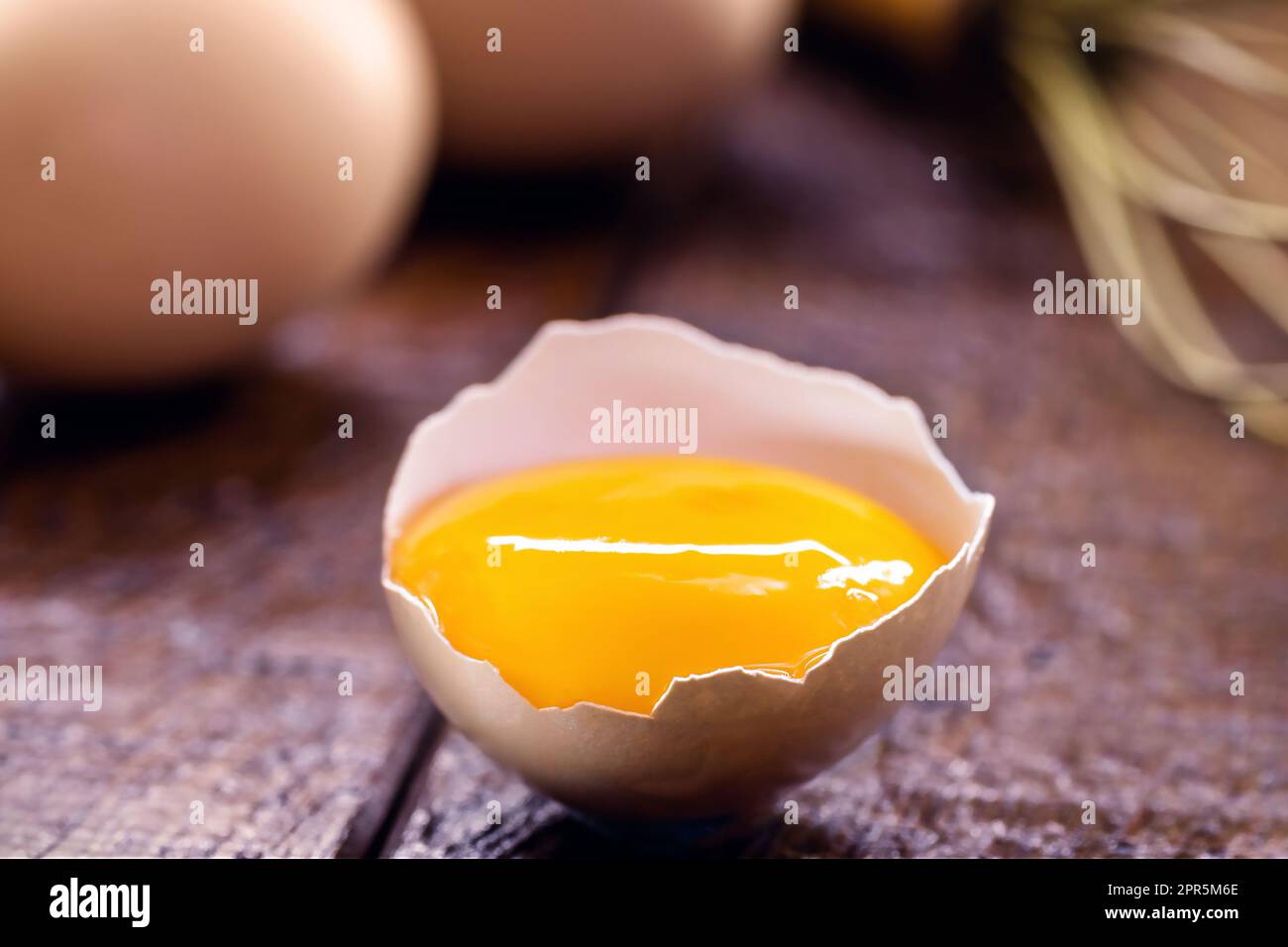 Zerbrochenes Hühnerei, sichtbares Eigelb auf Holztisch, Kochen mit Bio-Eiern Stockfoto