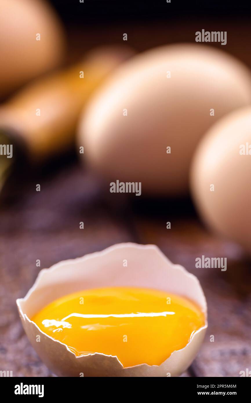 Zerbrochenes Hühnerei, sichtbares Eigelb auf Holztisch, Kochen mit Bio-Eiern Stockfoto