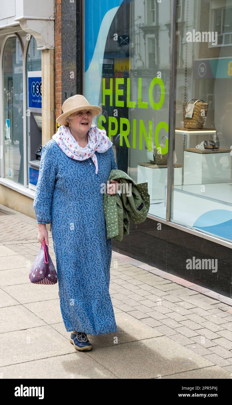 Eine ältere Dame, die für den Frühling gekleidet ist, hat ein Schaufenster mit dem Aufdruck Hello Spring Stockfoto