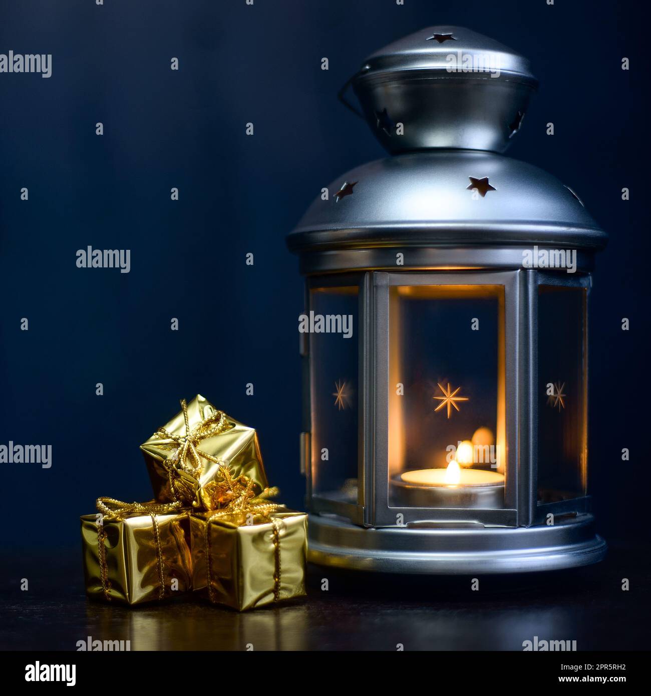Weihnachtskarte: Laterne mit Kerzen, leuchtend glänzende Schachteln mit Geschenken auf dunkelblauem Hintergrund. Stockfoto