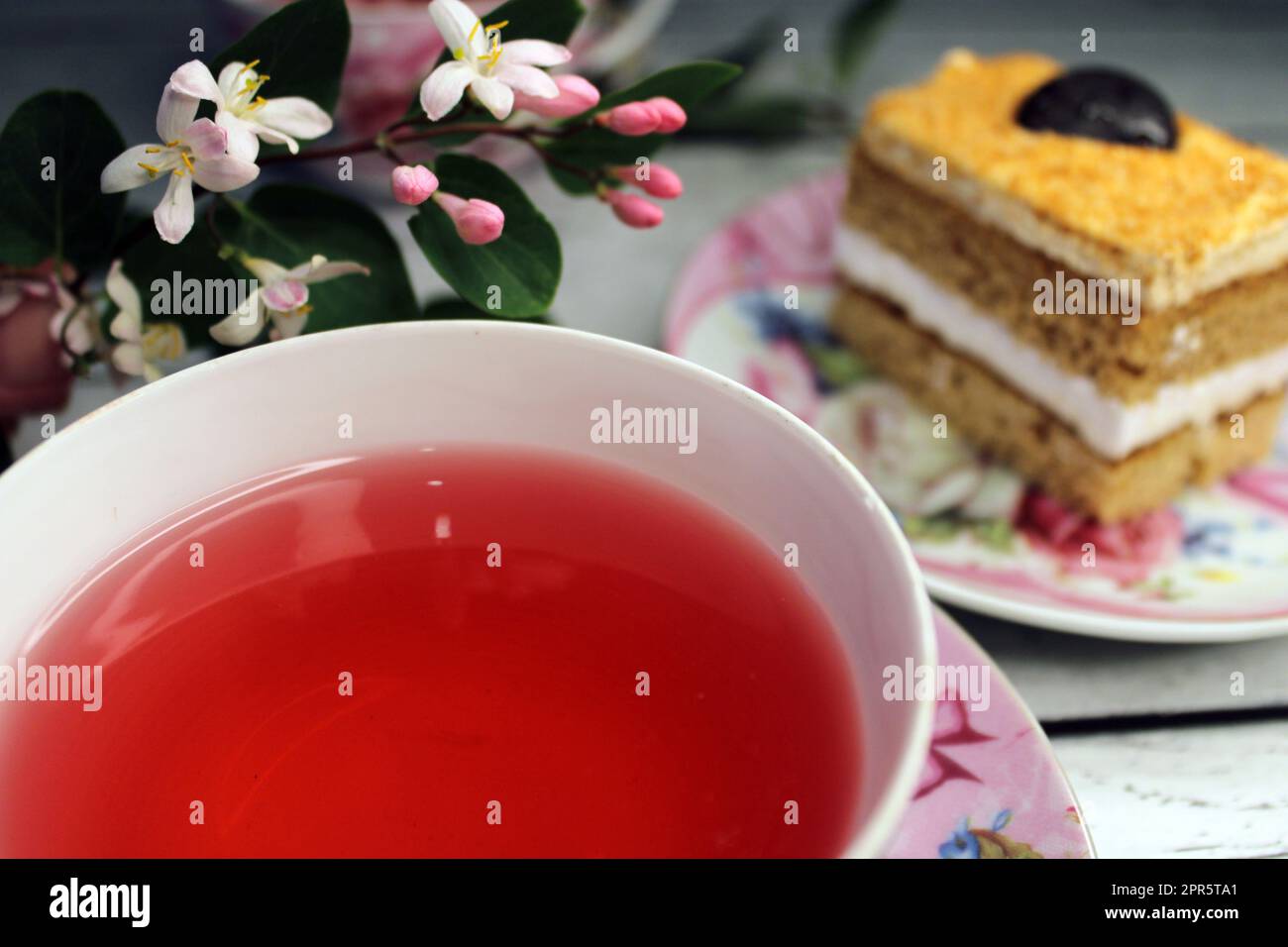 Eine Tasse Tee, groß, glatt und ein Kuchen auf einem Holztisch mit Blumen im Hintergrund Stockfoto