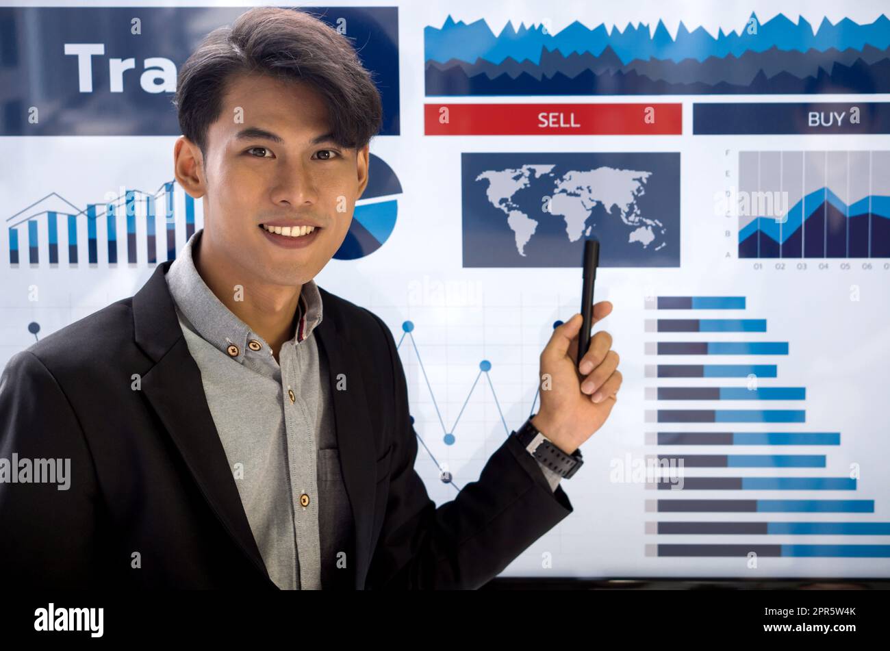Junger asiatischer Geschäftsmann in schwarzem Anzug, der auf die globale Karte auf dem Präsentationsmonitor zeigt. Stockfoto