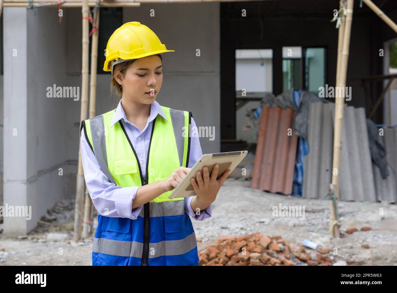Junger Ingenieur in einem Bauhelm und einer Sicherheitsweste, der den Arbeitsplan auf einem Tablet-Computer überprüft. Arbeitsumfeld auf der Baustelle von Wohnungsbauprojekten. Stockfoto