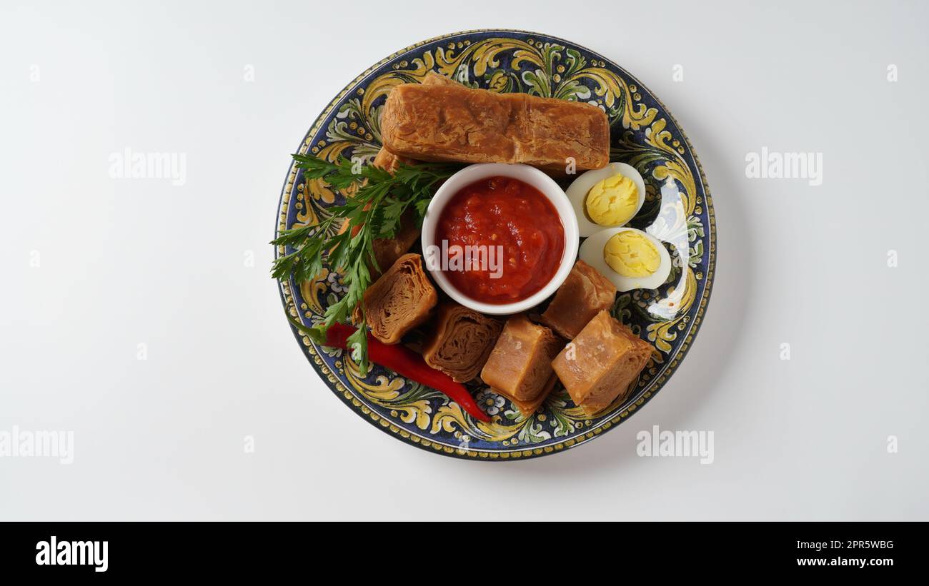 Jachnun oder Jahnun, jüdisches Gebäck aus dem jemenitischen Raum, serviert mit frischer geriebener Tomate und gekochtem Ei und Zhug, die von den Adeni-Juden stammen, und traditionell serviert am Sabbat-Morgen in Israel. Stockfoto