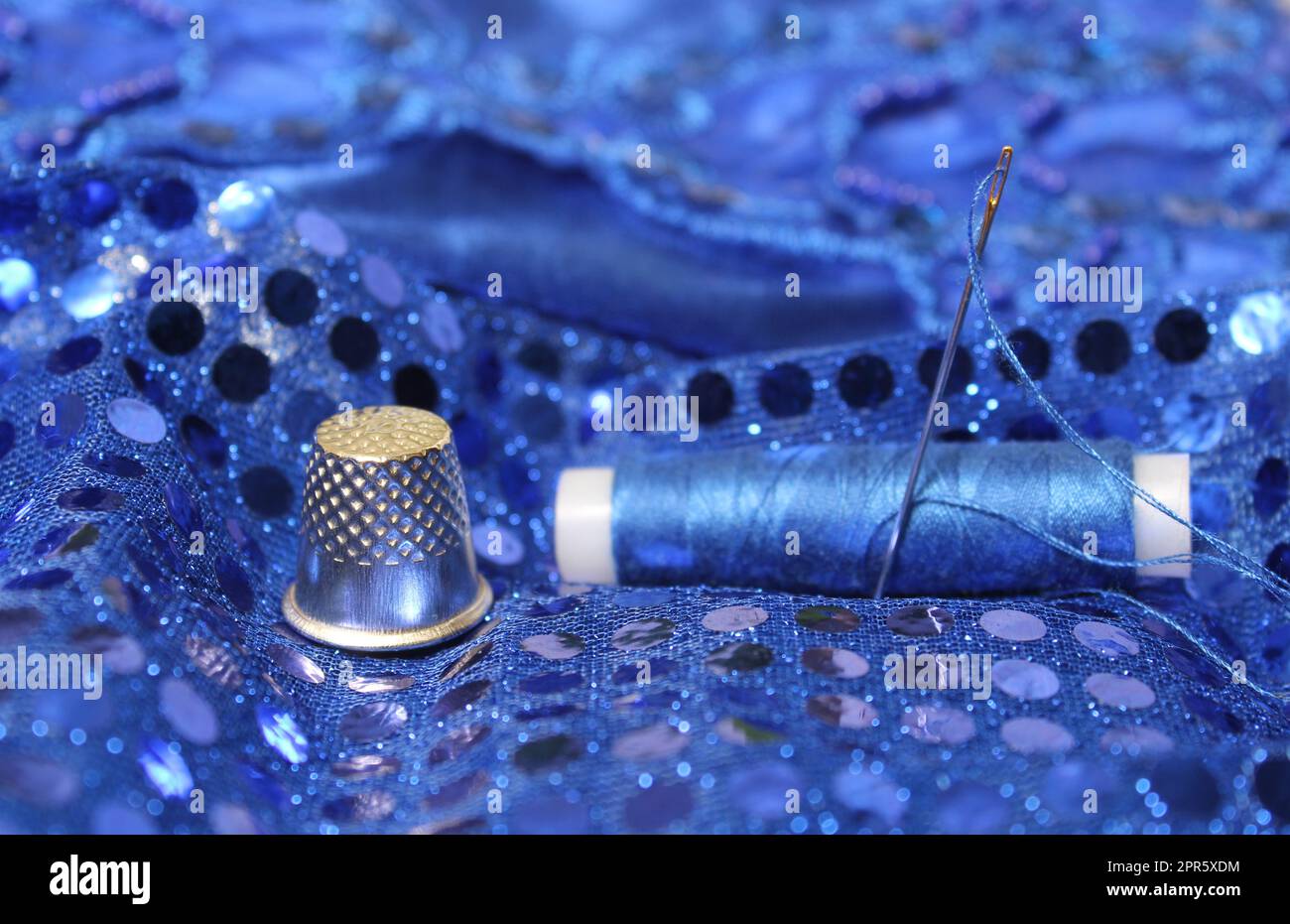 Blauer Faden mit Nadel und Fingerhut auf blauem Ballkleid Stockfoto