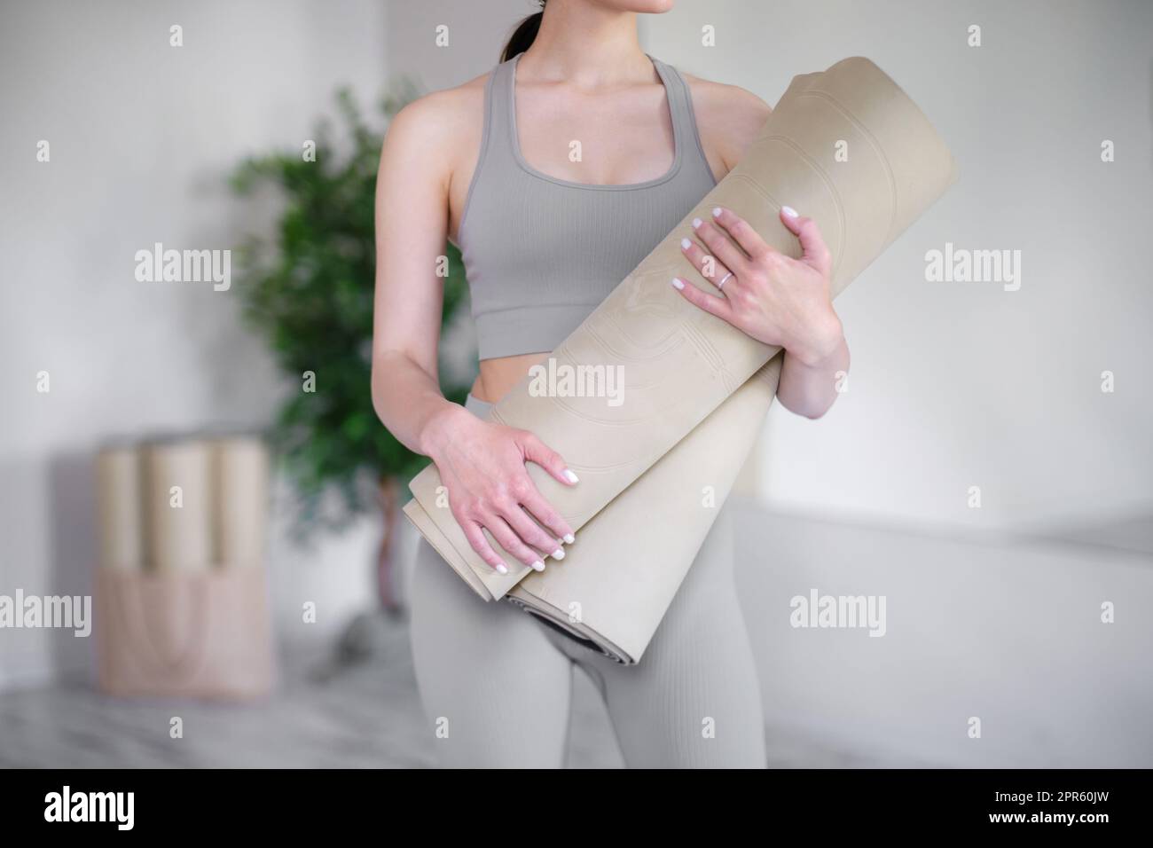 Junge Frau, die Yogamatten hält, während sie in einem hellen Studio steht. Stockfoto