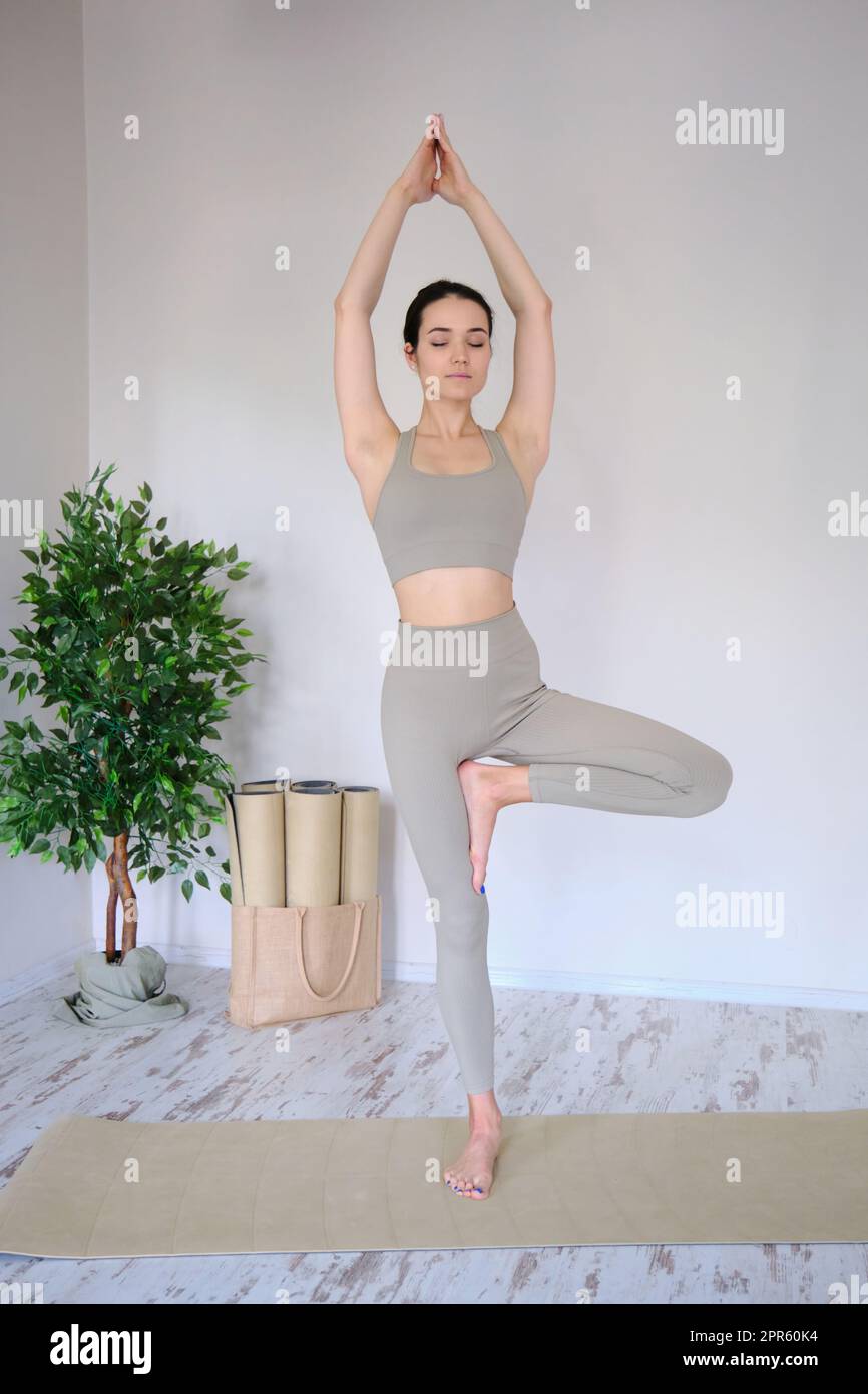 Eine junge, schöne Frau praktiziert Yoga in einem Studio, steht in einer Baumpose. Stockfoto