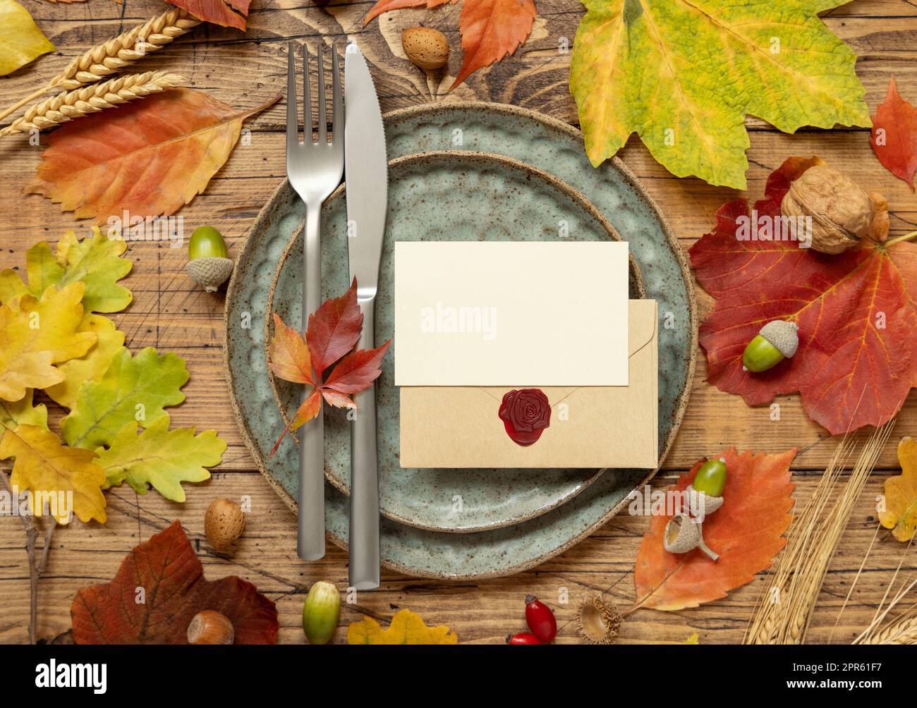 Rustikale Tischgestaltung im Herbst mit Karte und Umschlag zwischen Blättern und Beeren, Draufsicht, Modell Stockfoto