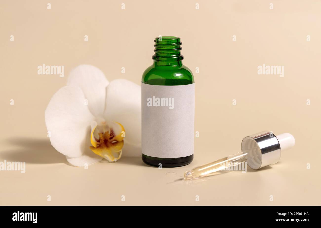 Grüne Tropfglasflasche neben weißen Orchideenblumen auf hellgelbem Mockup. Hautpflegeprodukt Stockfoto