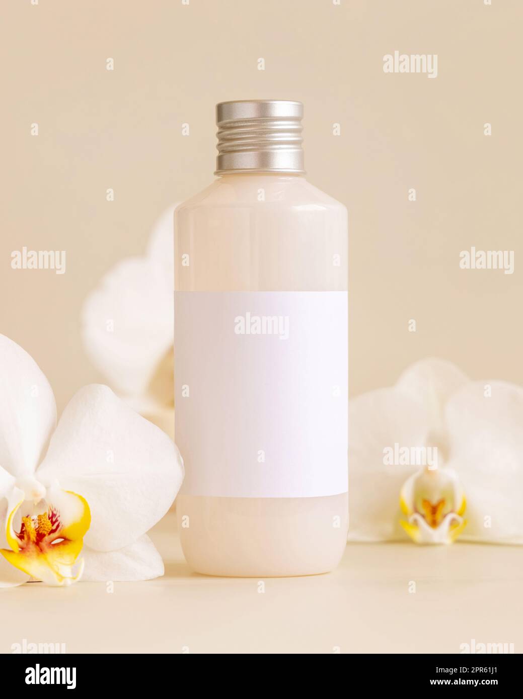 Kosmetikflasche mit leerem Etikett neben weißen Orchideenblumen auf hellgelbem Modell Stockfoto
