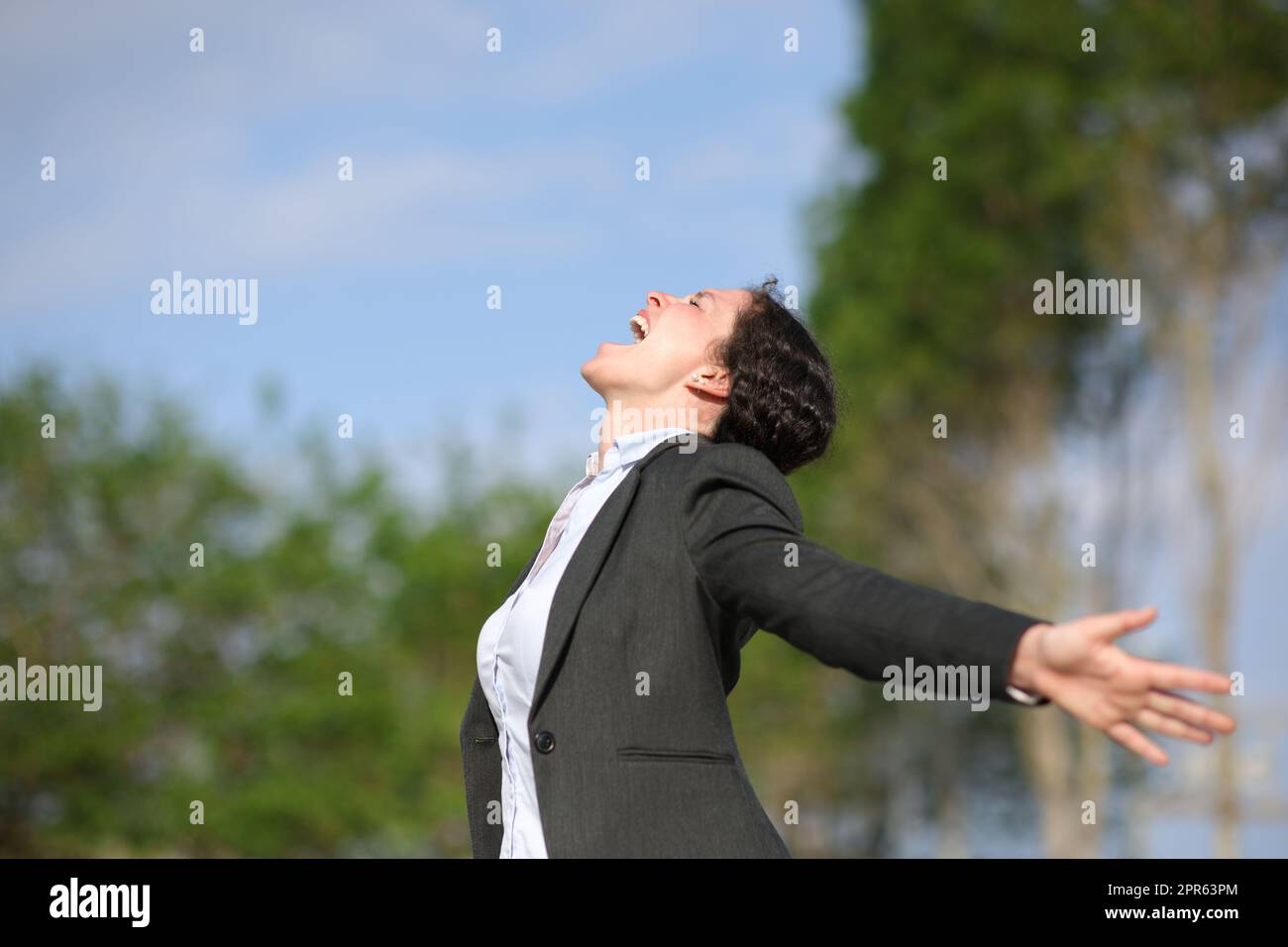 Aufgeregte Geschäftsfrau, die in einem Park die Arme überspannt Stockfoto