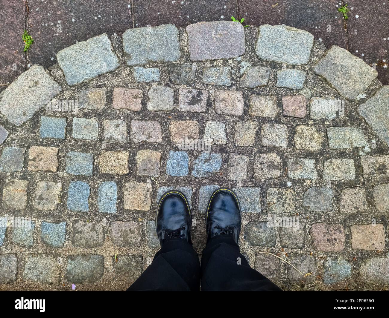 Zwei schwarze Schuhe und Beine auf einer Kopfsteinpflaster-Oberfläche - Draufsicht Konzept. Stockfoto