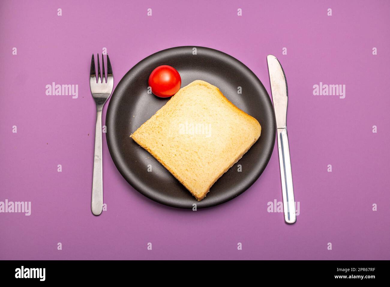 Teller mit Besteck, Tomate und Brotscheibe Stockfoto