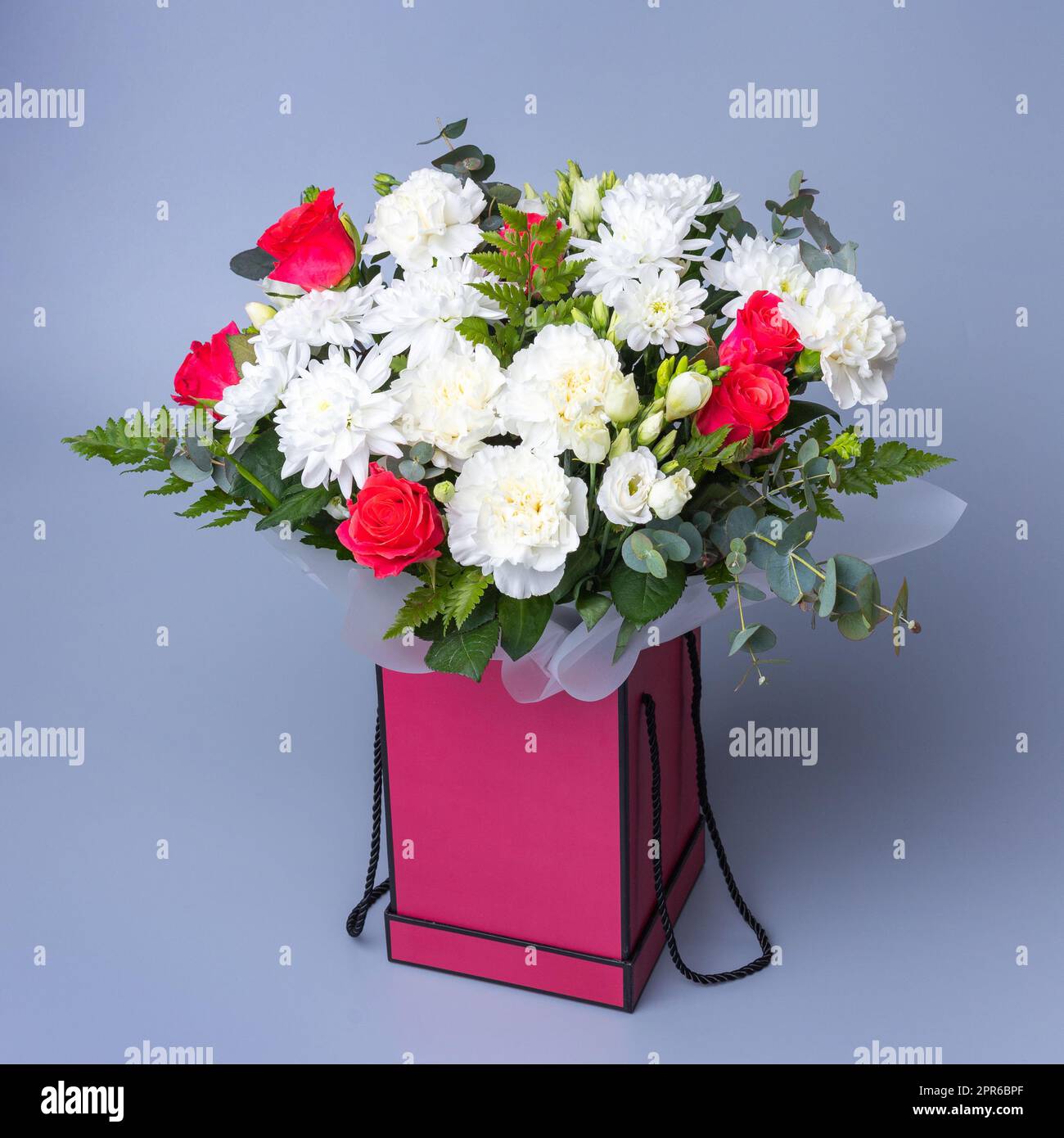 Wunderschöner Blumenstrauß in einer pinkfarbenen Geschenkbox auf blauem Hintergrund. Stockfoto
