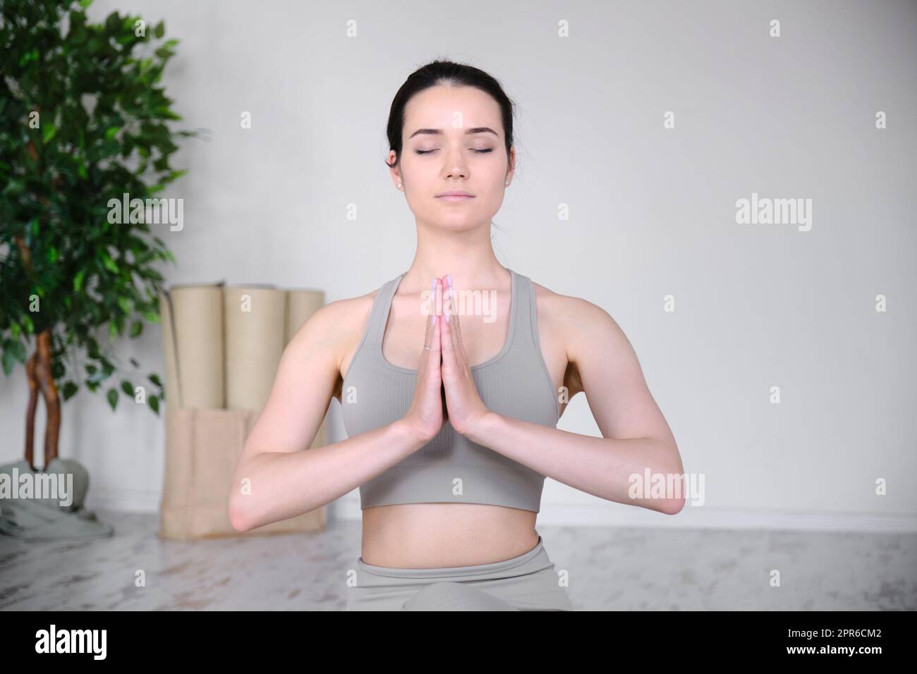 Porträt einer jungen Frau, die im Studio meditiert, während sie in einer halben Lotusposition auf einer Yogamatte sitzt. Stockfoto