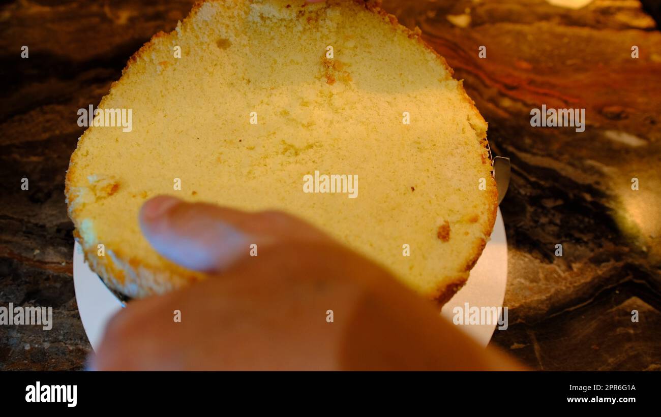 Ein männlicher Konditor stellt einen Kuchen auf Sahne mit Kirsche und presst ihn. Schlägt und flacht den Biskuitkuchen aus der Nähe Stockfoto