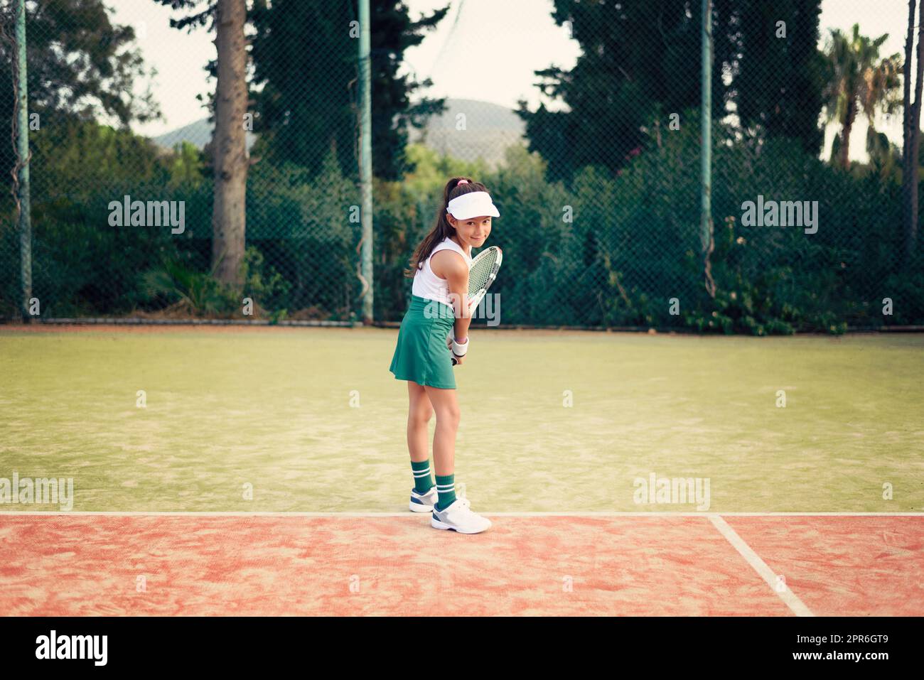 Junge Frau, Tennisspielerin mit grünem Rock, weißem Oberteil und Hut, die an einem sonnigen Tag Tennis auf einem Sandtennisplatz spielt Stockfoto