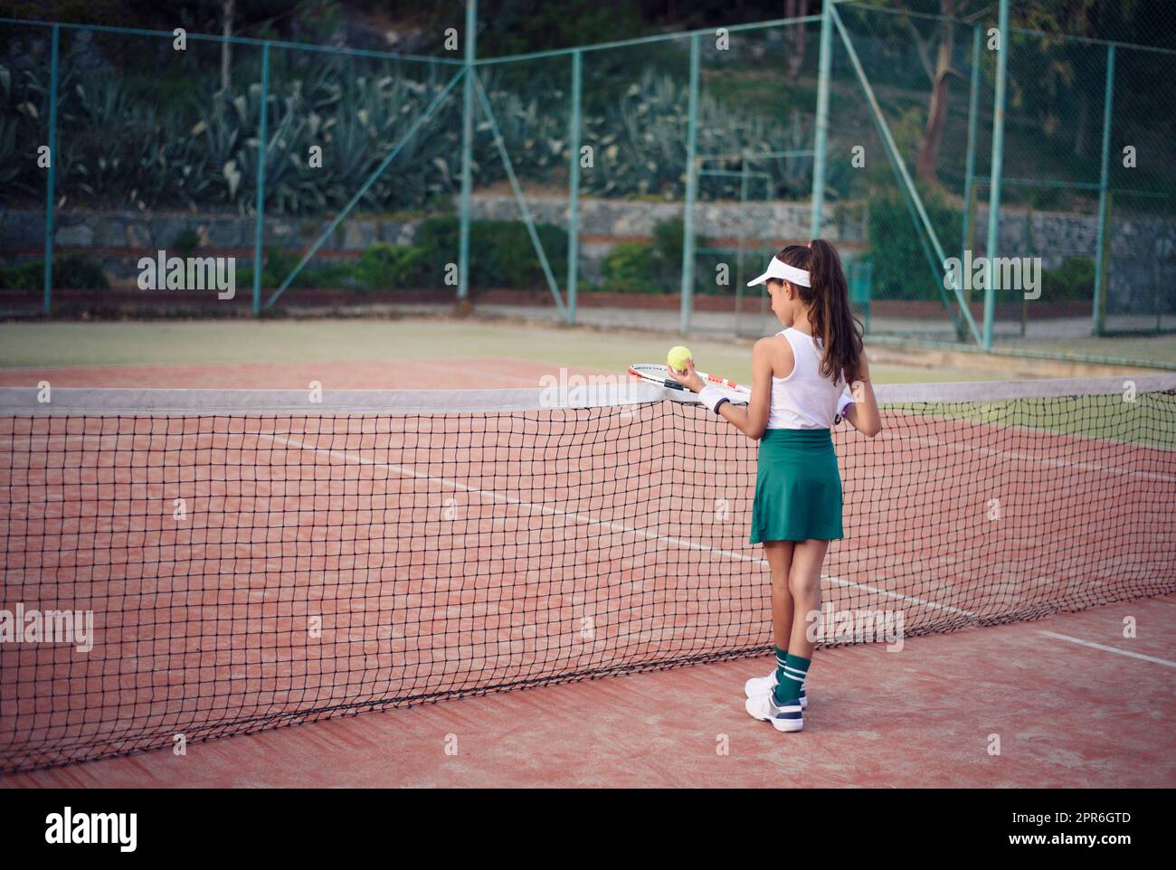 Junge Frau, Tennisspielerin mit grünem Rock, weißem Oberteil und Hut, die an einem sonnigen Tag Tennis auf einem Sandtennisplatz spielt Stockfoto