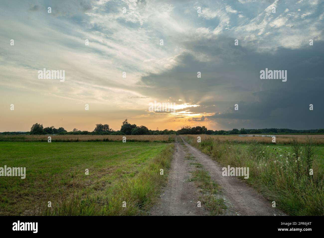 Ländliche Straße durch Felder und Wolken bei Sonnenuntergang Stockfoto