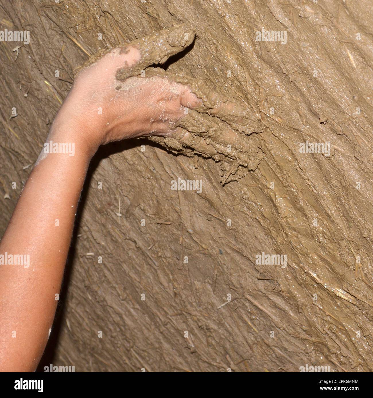 Hand einer jungen Frau, die eine ökologische Wand aus Lehm und Strohputz baut. Bauen mit natürlichem Material Stockfoto