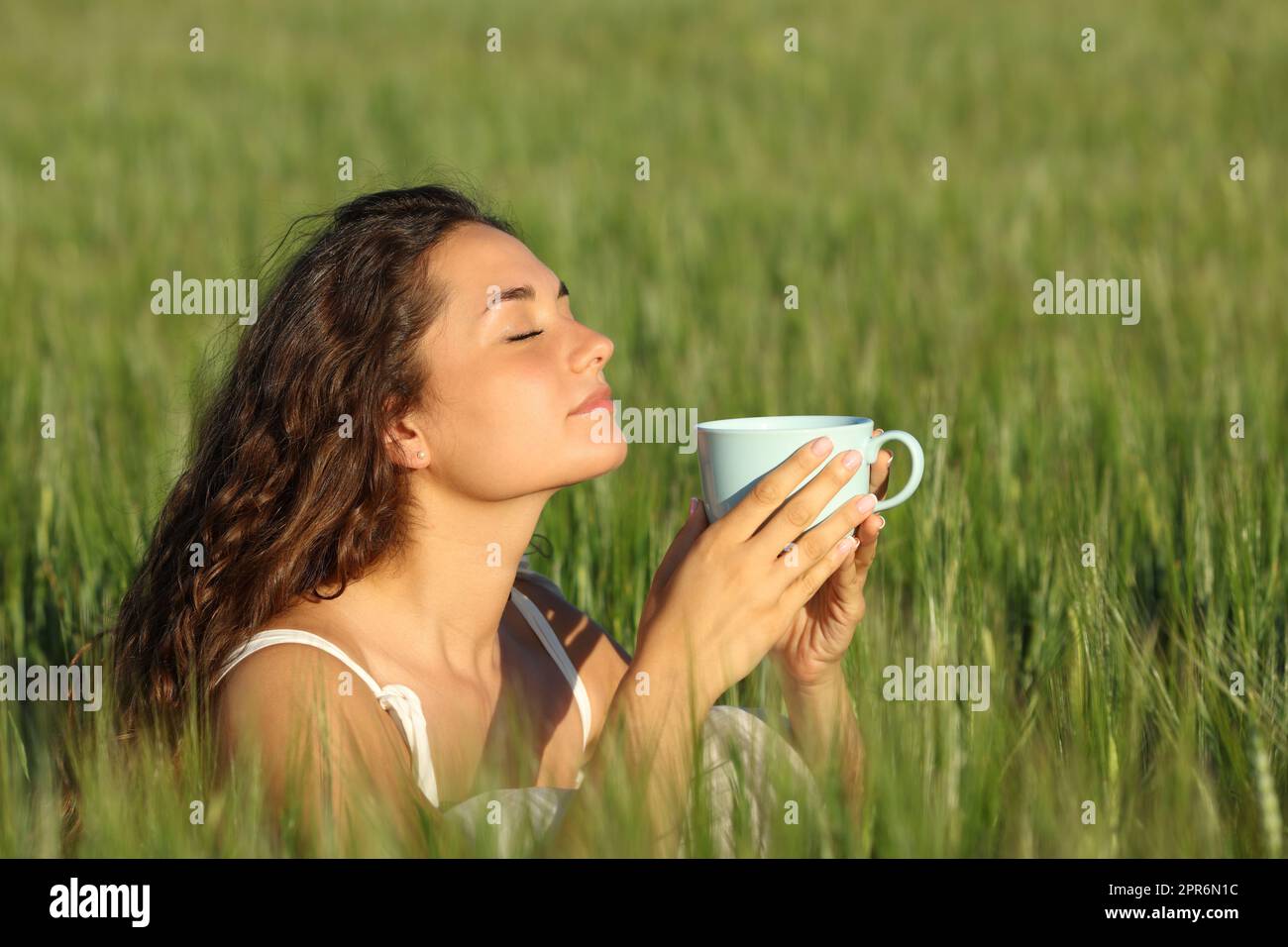 Eine Frau, die sich auf einem Weizenfeld entspannt und Kaffee riecht Stockfoto