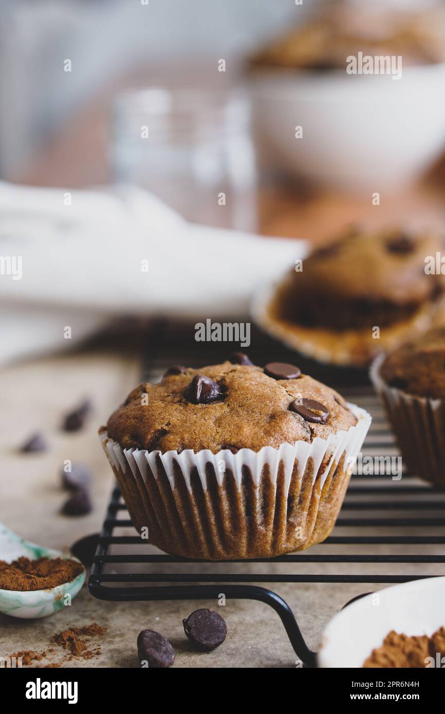 Veganer Kürbis-Schokochip-Muffin auf schwarzem Kühlgestell mit verstreuten Zutaten und Muffin-Verpackung, der den Hintergrund abblätterte. Stockfoto