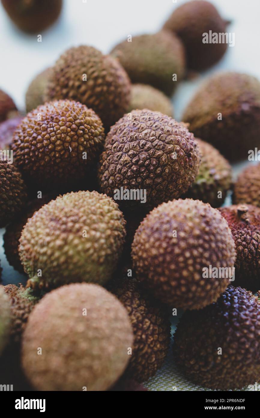 Nahaufnahme eines Haufens von violettem, strukturiertem Lychee, der auf einem braunen Holztisch sitzt. Stockfoto
