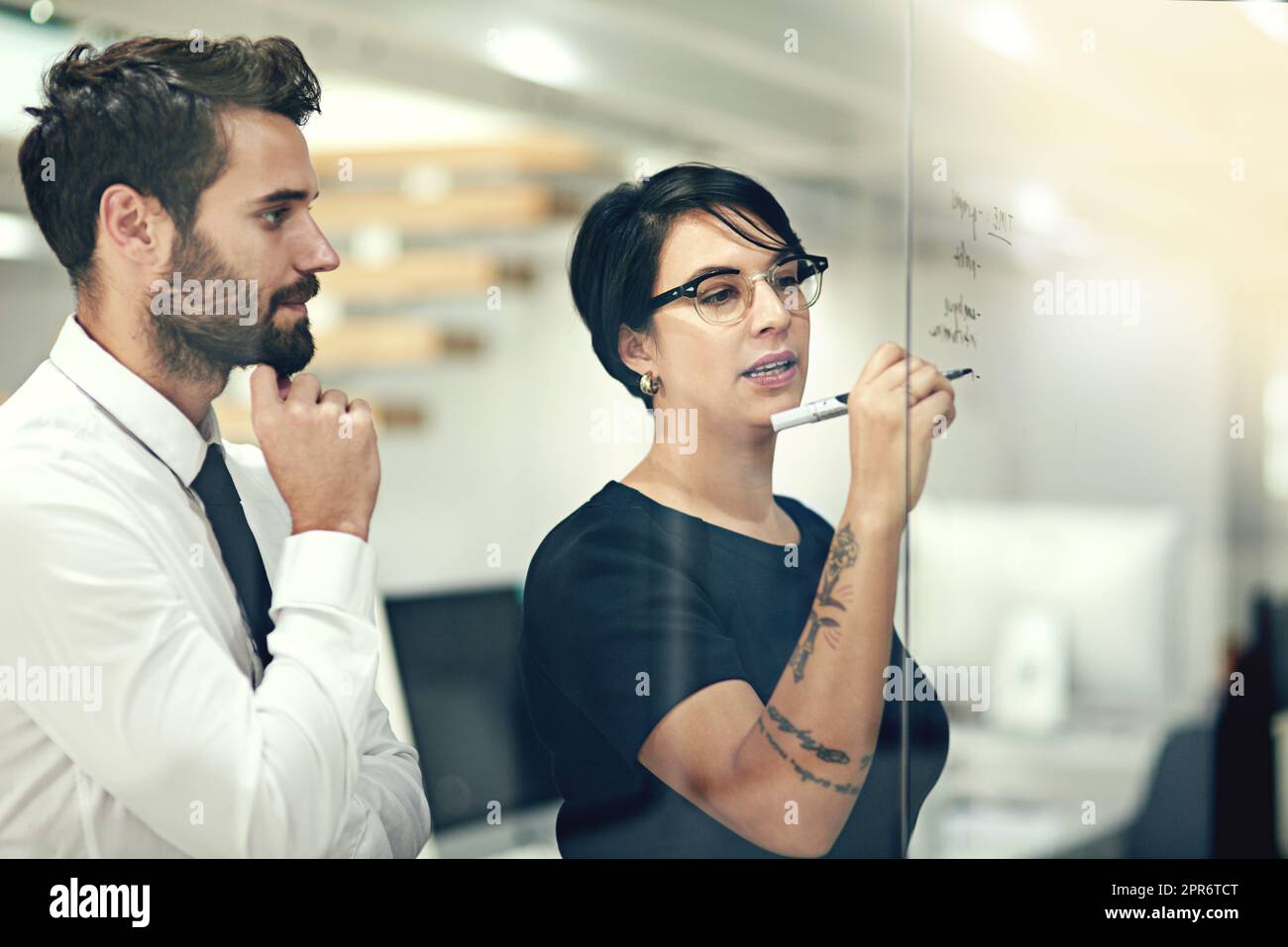 Unter Berücksichtigung aller Optionen. Eine kurze Aufnahme von Geschäftsleuten, die in einem Büro mit Notizen an einer Glaswand Brainstorming durchführen. Stockfoto