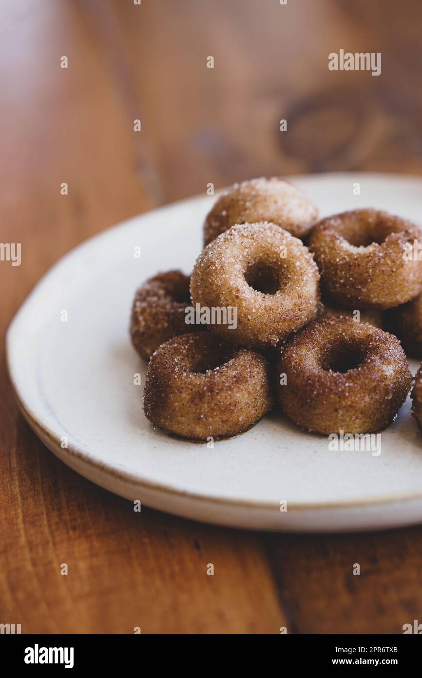 Ein Haufen veganer Mini-Zimt-Zucker-Donuts auf einer cremefarbenen Platte auf einem dunkelbraunen Holztisch. Stockfoto