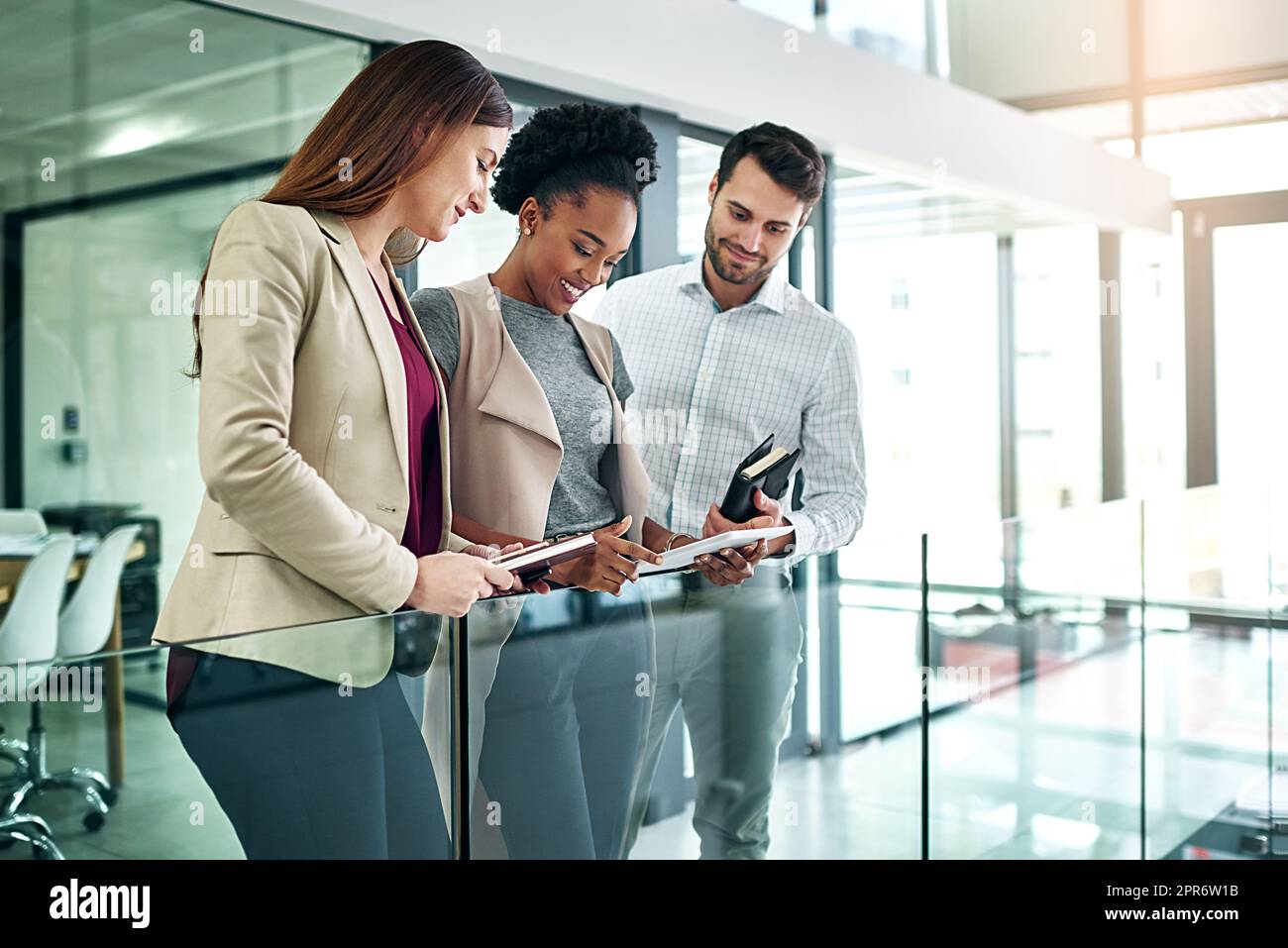 Gemeinsam ins Geschäft kommen. Aufnahme einer Gruppe von Kollegen, die sich über ein digitales Tablet unterhalten, während sie in einem großen, modernen Büro stehen. Stockfoto