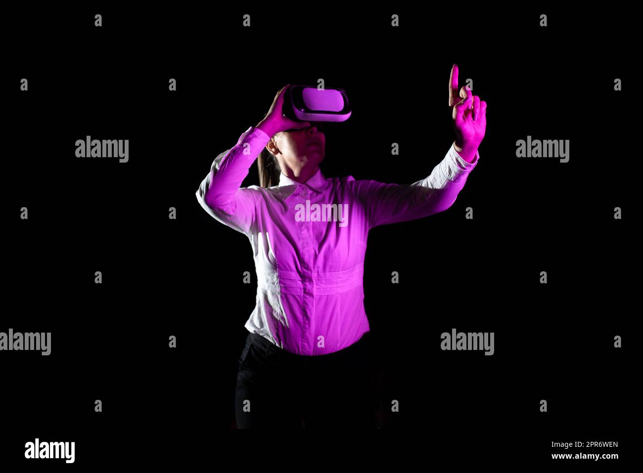 Geschäftsfrau, Die Eine Virtual-Reality-Brille Verwendet, Gesten Bei Der Teilnahme An Einer Professionellen Schulung. Das Licht Fällt Auf Eine Frau, Die Einen Modernen Simulator Trägt Und Kreative Technologie Präsentiert Stockfoto