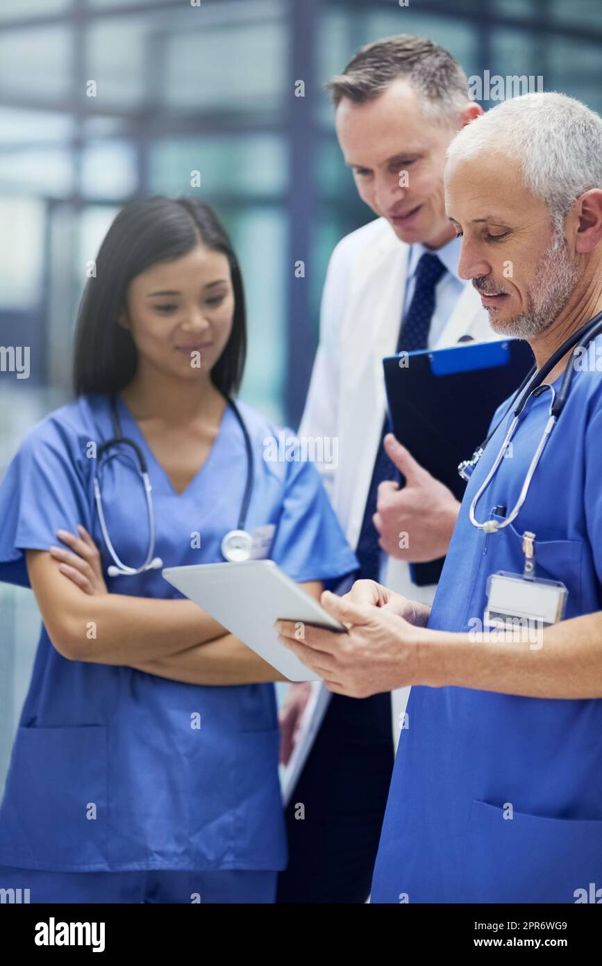 Dies sind einige vielversprechende Ergebnisse. Aufnahme einer Gruppe von Ärzten, die sich über ein digitales Tablet unterhalten, während sie in einem Krankenhaus stehen. Stockfoto