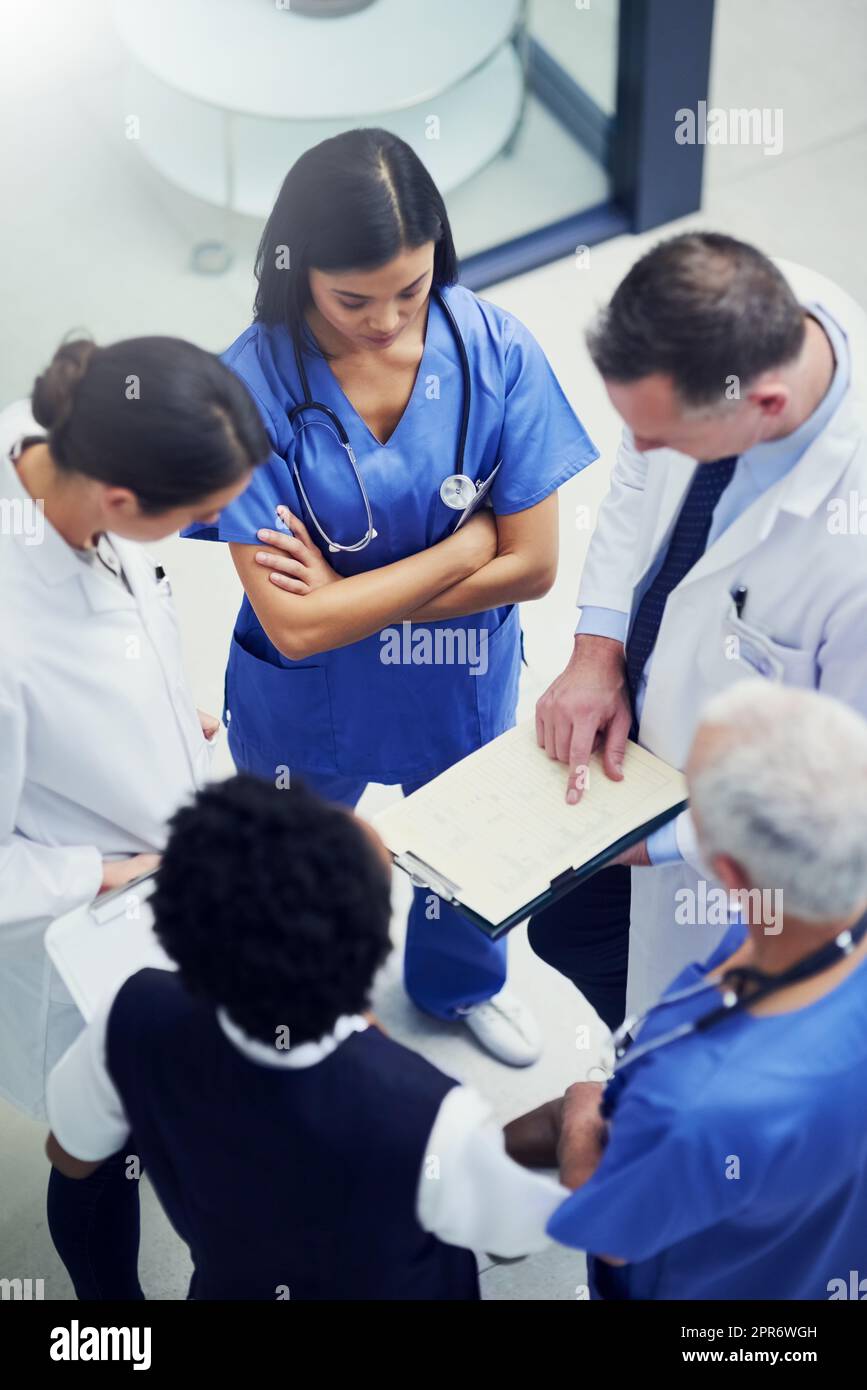 Gemeinsam werden sie eine Heilung finden. Aufnahme einer Gruppe von Ärzten, die sich über eine Krankenakte unterhalten, während sie in einem Krankenhaus stehen. Stockfoto