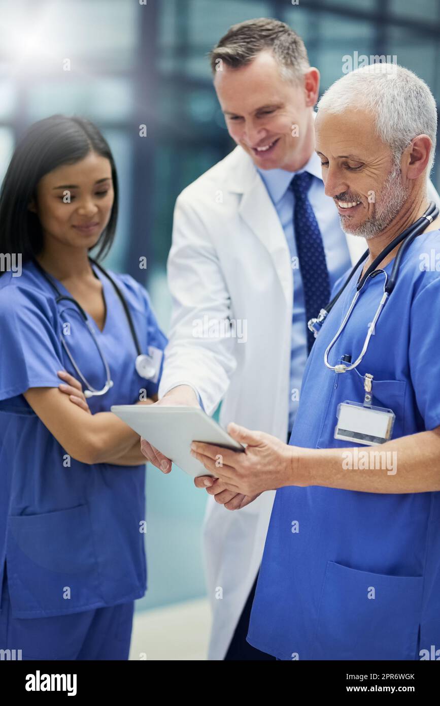 Leben retten durch Diagnose zu einem Zeitpunkt. Aufnahme einer Gruppe von Ärzten, die sich über ein digitales Tablet unterhalten, während sie in einem Krankenhaus stehen. Stockfoto