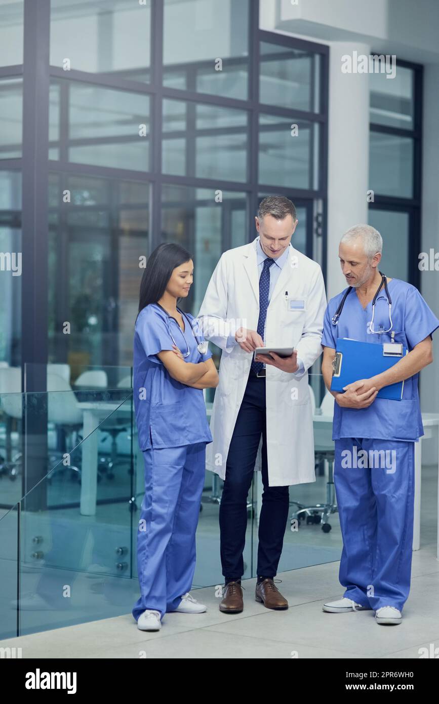 Diagnose vergleichen. Aufnahme einer Gruppe von Ärzten, die sich über ein digitales Tablet unterhalten, während sie in einem Krankenhaus stehen. Stockfoto