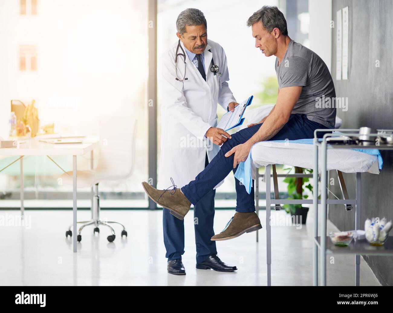 Ärzte tun es für die Gesundheit. Aufnahme eines reifen Arztes, der seinen Patienten untersucht, der sich um sein Knie sorgt. Stockfoto